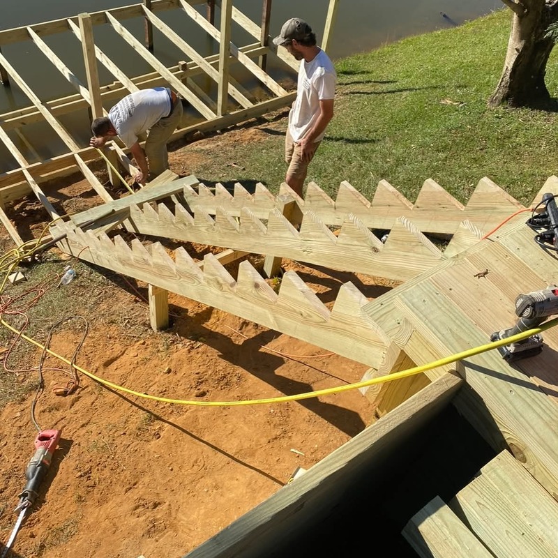 Contractors building a custom wooden deck beside a waterfront property