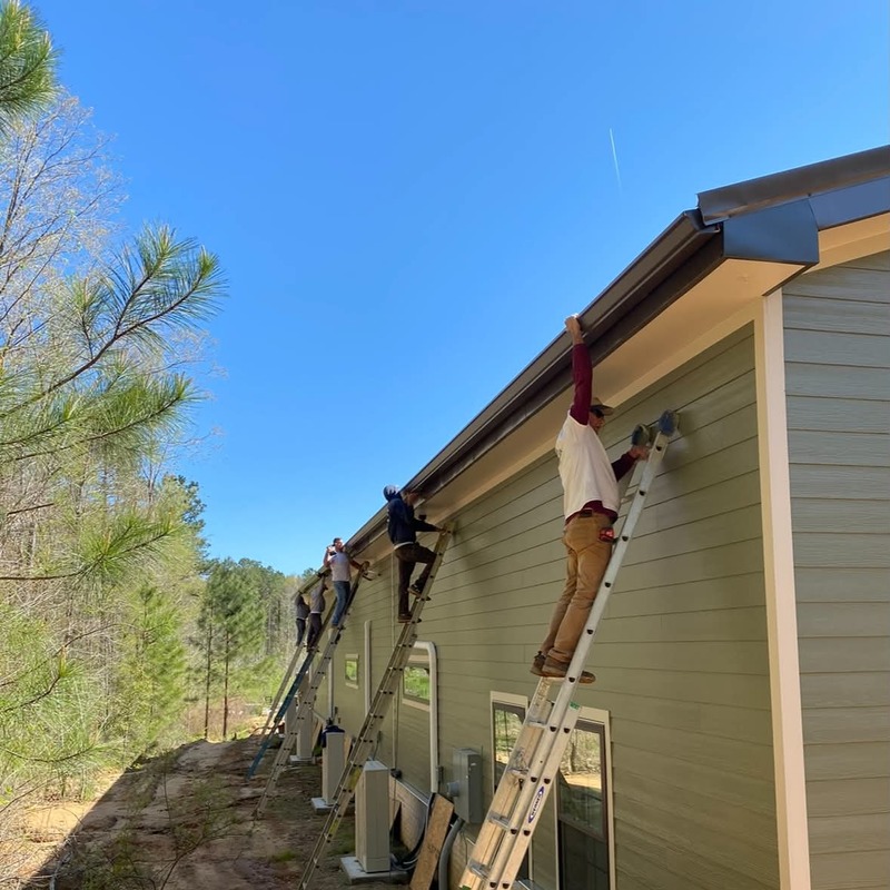 Crew installing rain gutters along the roofline of a residential home